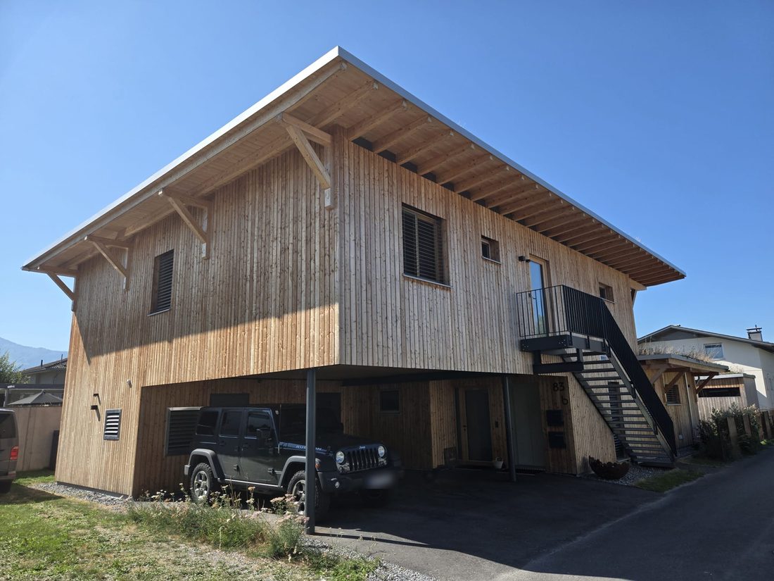 Zweigeschossiges Wohnhaus in Holzbauweise mit weit auskragendem Vordach, Balkon und Carport